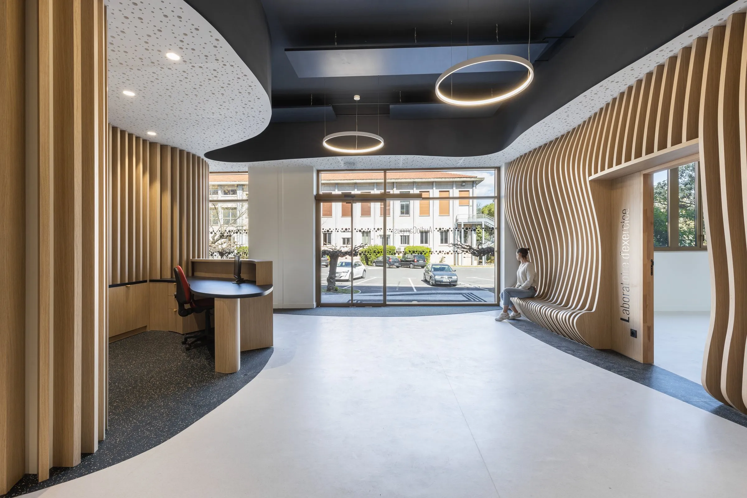 Hall avec claustra courbe en chêne, banque d'accueil et anneaux lumineux